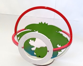 May include: A wooden, red, white, and green Poké Ball ornament. The Poké Ball is open and has a green palm tree inside.