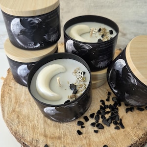 Peut inclure: Quatre bougies cylindriques noires avec des couvercles en bois clair. Les étiquettes présentent un motif de corbeau et de lune. La cire blanche est surmontée d'une lune en cire, d'une breloque pentacle argentée et de pierres noires.