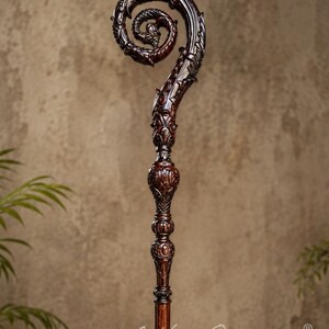 May include: A dark brown wooden staff featuring an intricate, carved spiral top with dragon-like motifs and detailed scrollwork. The shaft includes decorative, rounded nodes below the head, with the text Arthur Overseas printed at the bottom.