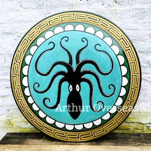 May include: A round, decorative shield featuring a teal background with a black octopus design. The shield has a gold and green border with a Greek key pattern and white accents. The text "Arthur Overseas" is visible.