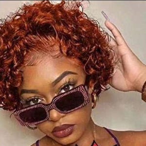 Puede incluir: Primer plano de una persona con gafas de sol rectangulares con pedrería rosa. La persona tiene el pelo corto, rizado y castaño rojizo y maquillaje oscuro. Las gafas de sol tienen lentes oscuras y montura rosa. La persona lleva un top morado.