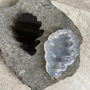 Puede incluir: Dos moldes de silicona para fundición de resina, uno negro y uno transparente, con forma de hoja con borde ondulado.