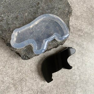 May include: A clear silicone mold shaped like a bear, with a black resin bear casting next to it.