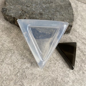 May include: A clear silicone mold shaped like a triangle. The mold is sitting on a gray surface. A black triangle is next to the mold.