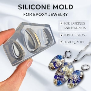 以下が含まれることがあります： エポキシ樹脂ジュエリーを作るためのシリコンモールド。モールドには、涙滴型のくぼみが3つあります。画像には、乾燥花が入った完成したエポキシペンダントも3つ表示されています。