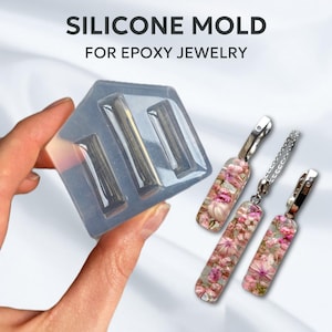 May include: Silicone mold for making rectangular epoxy jewelry. The mold is clear and has three rectangular cavities. The image also shows three finished epoxy jewelry pieces with pink floral designs.