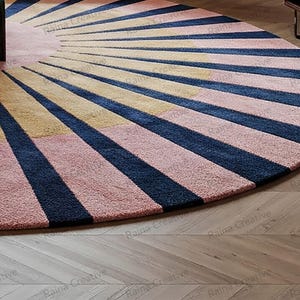 Round sunburst rug in navy, mustard, and pink wool blend; hand-tufted, 9ft modern boho living room rug on wood floor.