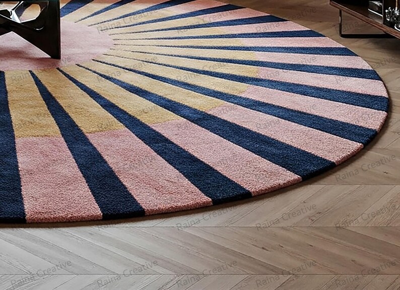 Round sunburst rug in navy, mustard, and pink wool blend; hand-tufted, 9ft modern boho living room rug on wood floor.