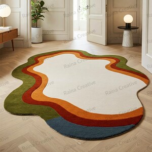 May include: A white, green, orange, and blue abstract area rug with a wavy, organic shape. The rug has a white center with three bands of color around the edge.