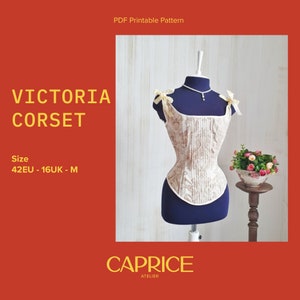 May include: A white and beige corset with a floral pattern, featuring a square neckline and adjustable straps. The corset is displayed on a mannequin against a woodgrain background. The text "VICTORIA CORSET" and "CAPRICE ATELIER" is visible in the image. The size is listed as "42EU - 16UK - M".