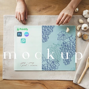 May include: A blue and white glass cutting board with a grapevine design. The board is on a beige linen surface with a wooden spoon and garlic cloves.