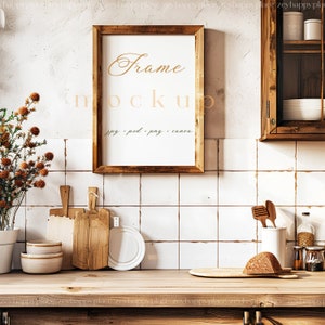 Op de afbeelding: Een rustieke keuken met een houten frame-mockup die aan een witte betegelde muur hangt. Het frame is leeg en klaar voor uw ontwerp. Het aanrecht is van hout en heeft een verscheidenheid aan keukengerei, waaronder snijplanken, kommen en een brood.