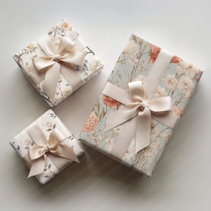 May include: Three wrapped gifts with floral patterned paper and cream-colored satin ribbons. The gifts are in varying sizes, with the largest featuring a light blue background and peach-colored flowers.
