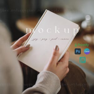 May include: A white notebook mockup with the text "mockup" and "jpg, png, psd, canva" written on it. The notebook is being held by a person's hands.