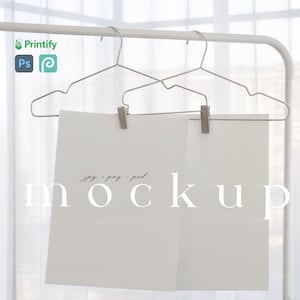 May include: A mockup image featuring two white paper sheets clipped to metal hangers. The word "mockup" is displayed in large, light-colored letters. The image includes the Printify logo and file type indications: jpg, png, and psd.