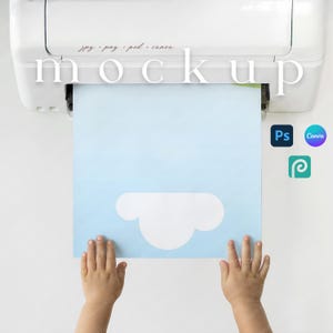 May include: A white printer with the word "mockup" printed on it. A light blue paper with a white cloud design is coming out of the printer. The paper is being held by two small hands. The image also includes the text "jpg. png. psd. canva."