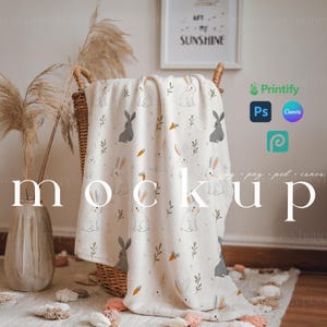 May include: A white throw blanket with a repeating pattern of gray bunnies and carrots. The blanket is folded and draped over a wicker basket.