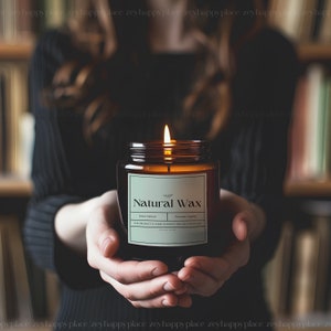 Pu&ograve; includere: Una candela di vetro marrone con un'etichetta bianca su cui &egrave; scritto "Natural Wax" in un carattere verde. La candela &egrave; accesa e la fiamma &egrave; visibile. La candela &egrave; tenuta dalle mani di una persona.