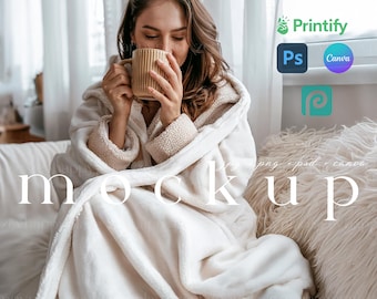 May include: A woman wearing a white hooded blanket sits on a couch and holds a beige mug. The blanket is soft and fluffy, and the woman looks cozy and relaxed. The background is blurred, and the image is a mockup for a product.