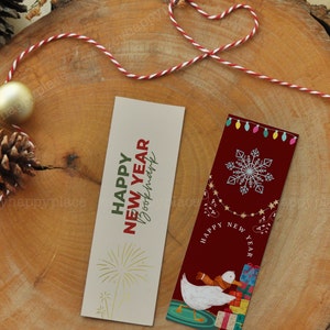 Puede incluir: Dos marcadores coloridos con saludos de A&ntilde;o Nuevo. El primer marcador es beige con texto dorado que dice "Happy New Year" y un dise&ntilde;o de fuegos artificiales dorados. El segundo marcador es rojo con un copo de nieve blanco, un pato blanco que lleva regalos y el texto "Happy New Year".