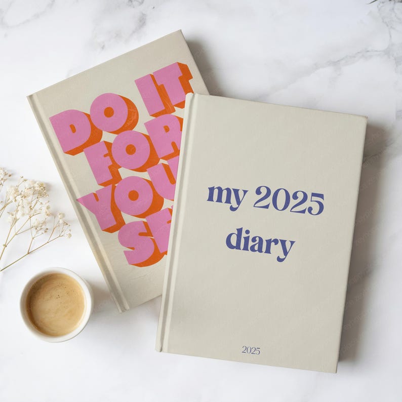 May include: Two hardback diaries with cream covers. One features the text "DO IT FOR YOU, SH*T" in pink and orange. The other reads "my 2025 diary" in blue, with "2025" at the bottom. A cup of coffee is also visible.