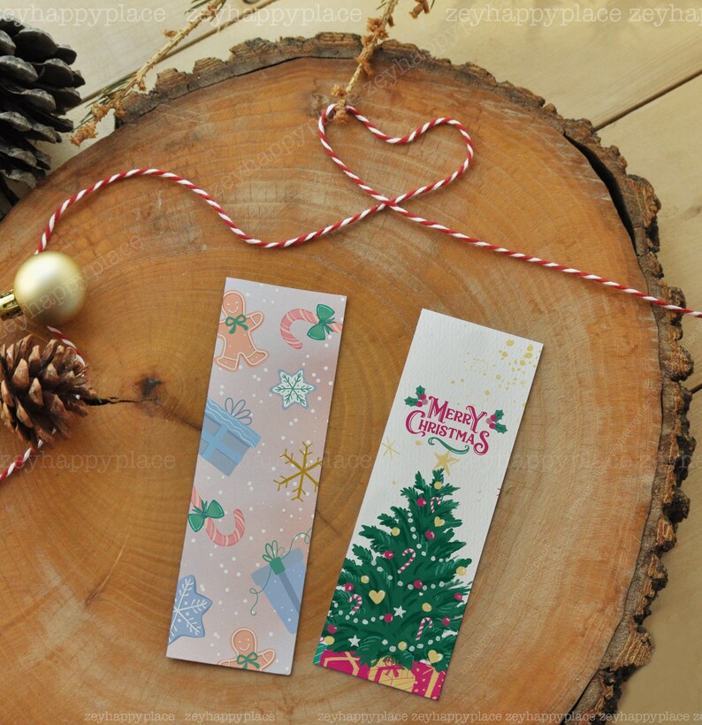Puede incluir: Dos marcap&aacute;ginas con tem&aacute;tica navide&ntilde;a. Un marcap&aacute;ginas presenta un fondo rosa y azul con hombres de jengibre, bastones de caramelo, copos de nieve y regalos. El otro marcap&aacute;ginas presenta un &aacute;rbol de Navidad verde con adornos rojos y blancos, bastones de caramelo y una pancarta roja con el texto "Feliz Navidad".