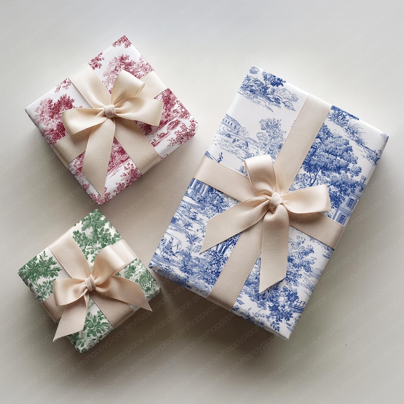May include: Three wrapped gifts with cream-colored bows. The wrapping paper features different patterns: a red and white toile, a blue and white landscape, and a green and white floral design. The gifts are arranged on a light background.