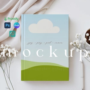 K&ouml;nnte beinhalten: Ein wei&szlig;es Notizbuch-Mockup mit einem Design aus blauem Himmel und gr&uuml;nen H&uuml;geln. Das Notizbuch tr&auml;gt den Text "jpg - png - psd - canva mockup" auf dem Cover.