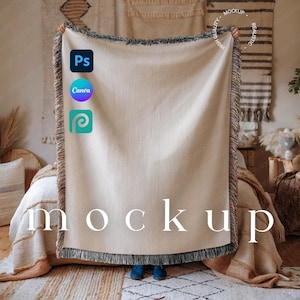 Könnte beinhalten: Eine cremefarbene gewebte Decke mit Fransen wird hochgehalten und zeigt das Wort "Mockup" in einer Serifenschrift. Die Decke wird in einem Schlafzimmer gezeigt. Die Decke hat einen dunkelgrauen Fransenrand. Das Bild enthält auch die Logos für Photoshop, Canva und Placeit.