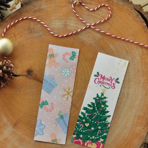 Puede incluir: Dos marcap&aacute;ginas con tem&aacute;tica navide&ntilde;a. El primer marcap&aacute;ginas tiene un fondo rosa con un patr&oacute;n de hombres de jengibre, bastones de caramelo, copos de nieve y regalos. El segundo marcap&aacute;ginas tiene un fondo blanco con un &aacute;rbol de Navidad verde decorado con adornos, bastones de caramelo y corazones. El texto "Feliz Navidad" est&aacute; escrito en rosa en el marcap&aacute;ginas.