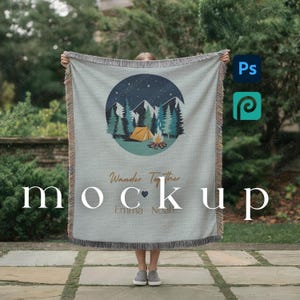 May include: A light gray woven blanket with a circular design featuring a mountain scene, trees, a tent, and a campfire. The text "Wander Together" and "Emma - Noah" are also visible. The blanket has fringed edges.