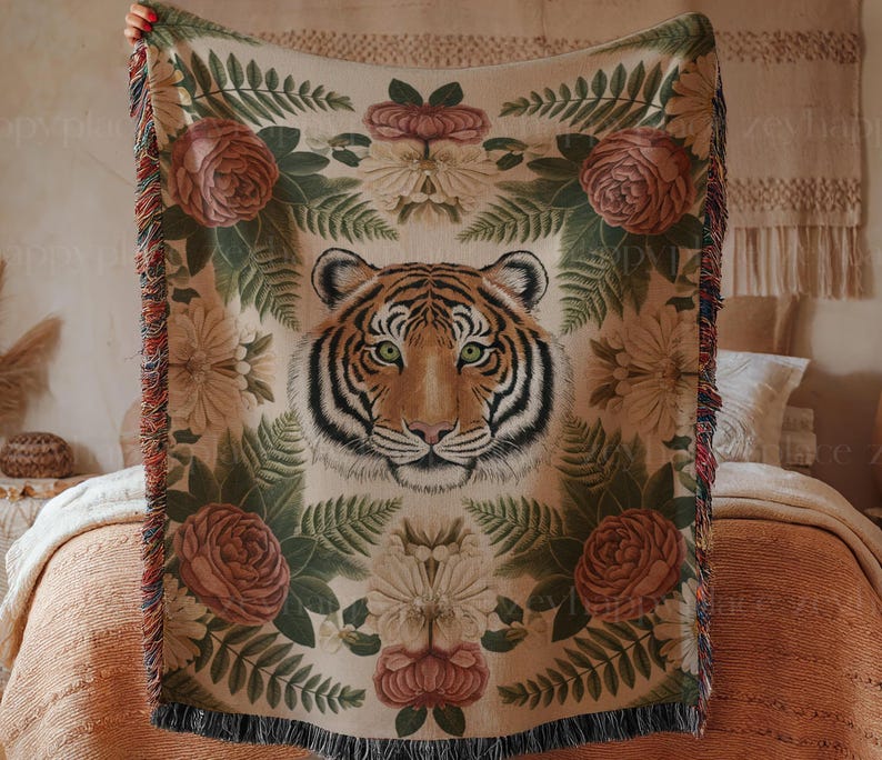 Puede incluir: Una manta de tiro de tapicer&iacute;a tejida presenta una cara de tigre rodeada de exuberante follaje verde y flores coloridas. La manta de tiro tiene un borde de flecos.
