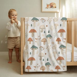 May include: A white baby blanket featuring a repeating pattern of mushrooms in brown, teal, and beige, with sprigs and leaves. The blanket is draped over a wooden cot.