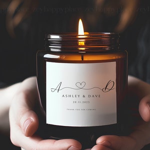 Pu&ograve; includere: Un barattolo di vetro marrone con una candela e un'etichetta bianca. L'etichetta riporta il testo "A & D" con un simbolo di cuore, "Ashley & Dave", "20.11.2023" e "Grazie per essere venuti".