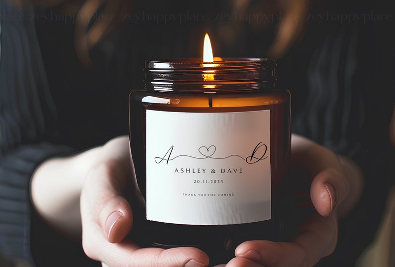 Pu&ograve; includere: Un barattolo di vetro marrone con una candela e un'etichetta bianca. L'etichetta riporta il testo "A & D" con un simbolo di cuore, "Ashley & Dave", "20.11.2023" e "Grazie per essere venuti".