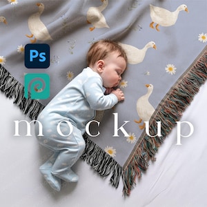 May include: A sleeping baby lies on a pale blue blanket decorated with white geese and daisies. The blanket has a fringed edge. The baby wears a light blue onesie with white polka dots. The word "mockup" is displayed.