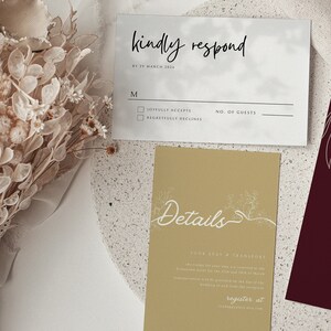 K&ouml;nnte beinhalten: Eine wei&szlig;e RSVP-Karte mit einem grauen Aquarellhintergrund. Der Text "kindly respond" ist in schwarzer Kursivschrift geschrieben. Die Karte enth&auml;lt ein Kontrollk&auml;stchen f&uuml;r "joyfully accepts" und "regretfully declines" mit einer Zeile f&uuml;r die Anzahl der G&auml;ste. Eine zweite Karte mit goldfarbenem Hintergrund und wei&szlig;em Blumenmuster enth&auml;lt den Text "Details" und Informationen &uuml;ber den Aufenthalt und den Transport. Der Text "register at" und eine Website-Adresse sind am unteren Rand der Karte enthalten.