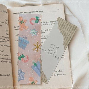 K&ouml;nnte beinhalten: Zwei Lesezeichen, eines mit rosa Hintergrund und einem winterlichen Urlaubsthema mit Lebkuchenm&auml;nnern, Schneeflocken und Zuckerstangen, und das andere mit grauem Hintergrund und dem Text "NEW DAY NEW CHAPTER".