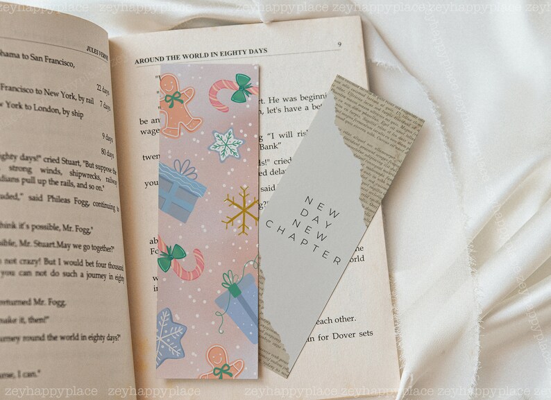 K&ouml;nnte beinhalten: Zwei Lesezeichen, eines mit rosa Hintergrund und einem winterlichen Urlaubsthema mit Lebkuchenm&auml;nnern, Schneeflocken und Zuckerstangen, und das andere mit grauem Hintergrund und dem Text "NEW DAY NEW CHAPTER".
