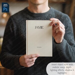 May include: A cream-colored journal with the name "JAMIE" printed at the top and the word "THOUGHTS" at the bottom. The journal is held by a person wearing a gray sweater. The image also includes a "Smart Object" layer with text.