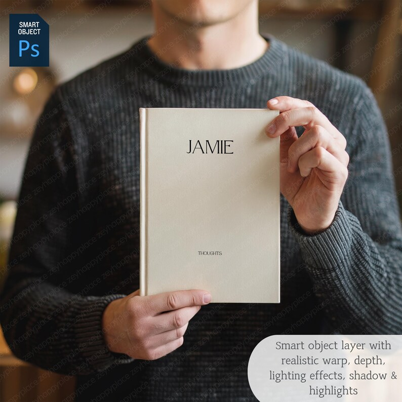 May include: A cream-colored journal with the name "JAMIE" printed at the top and the word "THOUGHTS" at the bottom. The journal is held by a person wearing a gray sweater. The image also includes a "Smart Object" layer with text.