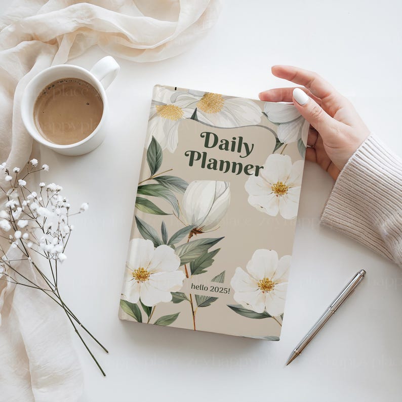 Puede incluir: Una agenda diaria beige con un dise&ntilde;o floral con flores blancas y hojas verdes. El texto "Daily Planner" est&aacute; impreso en verde en la portada. El texto "hello 2025!" est&aacute; impreso en negro en la parte inferior de la portada.