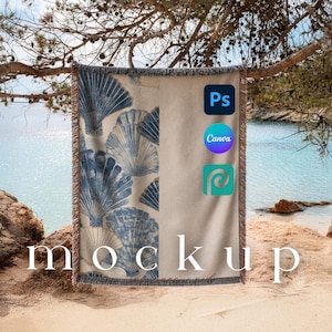 Könnte beinhalten: Eine beige und blau gemusterte Decke mit Muscheln und einem Fransenrand. Die Decke ist über einen Ast an einem Strand drapiert. Das Wort "Mockup" ist auf die Decke gedruckt.