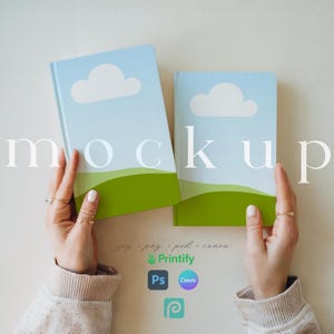 May include: Two hands hold up two blue and green notebooks with white clouds and the word "mockup" printed on them.