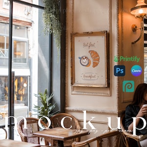 Puede incluir: Un póster enmarcado con fondo blanco y marco dorado. El póster presenta una ilustración de dibujos animados de una taza de café con un croissant y el texto "But first, breakfast". El póster está colgado en una pared en un ambiente de cafetería.