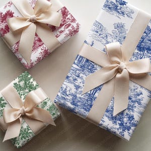 May include: Four wrapped gifts with cream-colored bows. The wrapping paper features various patterns: a red toile, a blue toile, and a green toile. The gifts are arranged on a neutral surface.