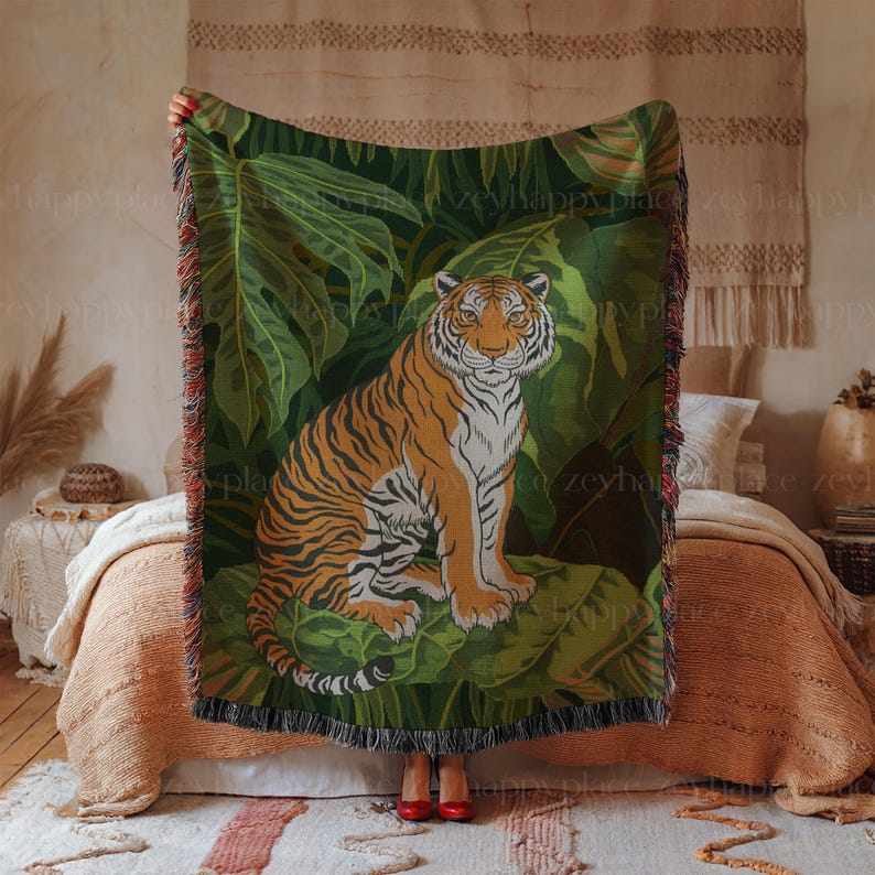 Puede incluir: Una manta tejida con un dise&ntilde;o de tigre verde, marr&oacute;n y naranja. El tigre est&aacute; sentado en un entorno de jungla con exuberantes hojas verdes.