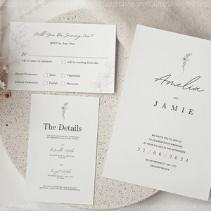K&ouml;nnte beinhalten: Eine Hochzeitseinladungssuite im minimalistischen Design. Die Einladung zeigt die Namen Amelia und Jamie in Kursivschrift mit einer kleinen floralen Illustration. Die Detailkarte enth&auml;lt das Datum, die Uhrzeit und den Ort der Hochzeit. Die RSVP-Karte enth&auml;lt einen Abschnitt, in dem die G&auml;ste ihre Essensvorlieben angeben k&ouml;nnen.