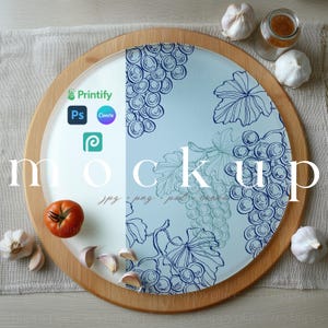 May include: A circular wooden chopping board with a glass insert displaying a blue grape pattern. A tomato, garlic cloves, and a small jar are arranged around the board. The word "mockup" is printed on the board.