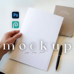 May include: A white paper mockup held by a hand, with the word "mockup" in large, elegant font. A pen and a "Work Planner" notebook are also visible. The image includes the logos for Photoshop and a design program.